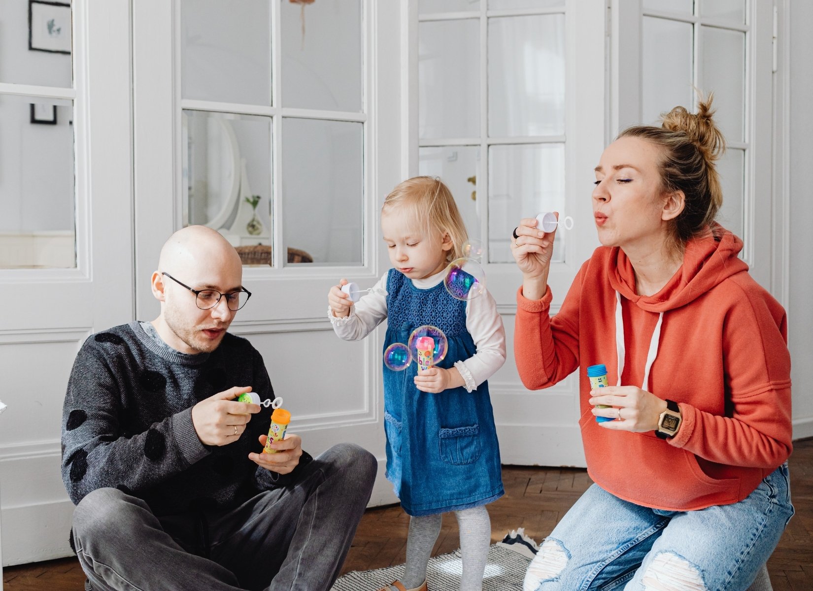 Mom, dad and child blow bubbles in a home.